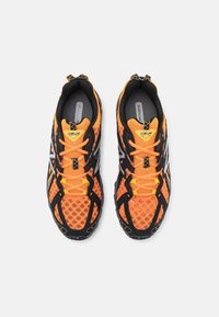 Orange nätträningsskor med svarta accenter, som har ett distinkt mönster på sulan, framträdande snören och reflekterande detaljer.