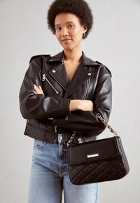 Veste de moto en cuir noir avec des zippers en argent, associée à un sac à main matelassé noir avec un rabat orné d'or et une bandoulière en chaîne.