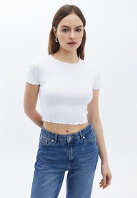 Hvid cropped top med korte ærmer, bølget halsudskæring og glat tekstur. Kombination med højtsiddende blå denimjeans.