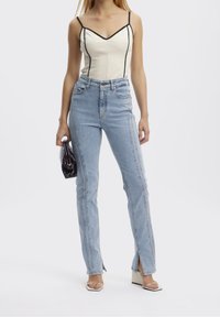 Jeans de tiro alto de color azul claro con aberturas laterales y costuras en contraste, combinados con una blusa ajustada color crema con ribetes negros y tirantes de espagueti.