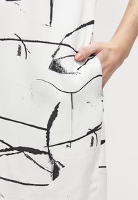 Abito bianco con audaci motivi astratti neri, dotato di una tasca laterale. Tessuto morbido, design a taglio morbido per il massimo comfort.