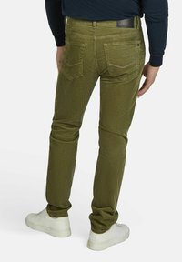 Olivgrüne Cordhosen mit slim Fit, Gesäßtaschen und einer dezenten Textur. Kombiniert mit weißen Sneakers für einen lässigen Look.