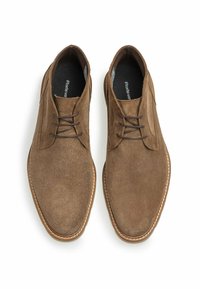 Zapatos de ante marrón con una textura suave, diseño de cordones y costuras blancas a lo largo de las suelas, con forma de punta redonda.