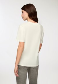 Koszulka z krótkim rękawem i okrągłym dekoltem w jasnym kremowym kolorze, o gładkiej fakturze. Połączona ze szarymi, dopasowanymi, teksturowanymi dżinsami.