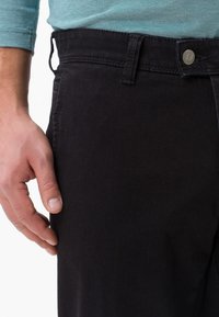 Pantaloni di jeans neri con una trama liscia, caratterizzati da una chiusura frontale con bottone e una tasca laterale, presentati su uno sfondo chiaro.