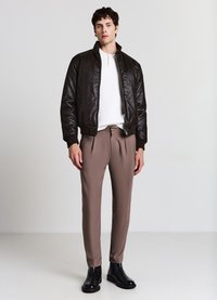 Braune Bomberjacke aus Kunstleder mit gerippten Bündchen, kombiniert mit beigefarbenen, maßgeschneiderten Hosen und schwarzen Knöchelstiefeln. Einfaches, elegantes Design.