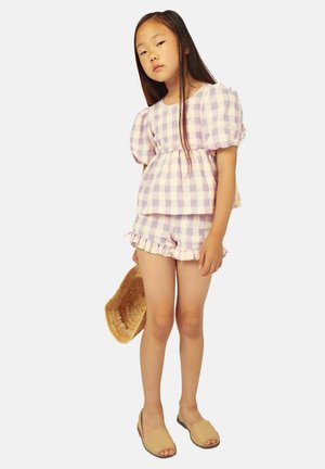Conjunto de dos piezas a cuadros en tonos morado claro y blanco, que incluye una blusa con mangas abullonadas y pantalones cortos con volantes, combinados con sandalias tipo slip-on en color beige.