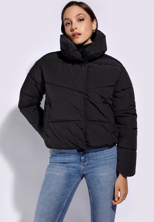 Giacca a vento nera con colletto alto, motivo a righe orizzontali e design cropped, abbinata a jeans in denim blu.