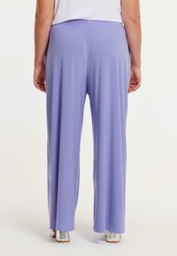 Lichtpaarse wijde broek met een gladde textuur en elastische tailleband, gezien vanaf de achterkant, gecombineerd met glanzende zilveren schoenen.