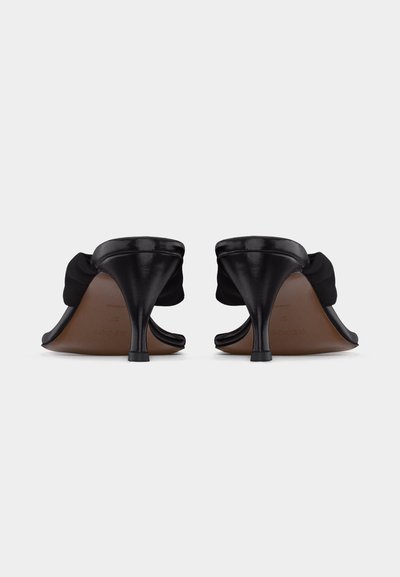 Pár čiernych dámskych sandálok na podpätku s tenkými podpätkami a detailom z látkového mašle, pohľad zozadu na bielom pozadí.