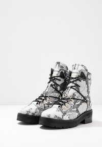 Botines de tobillo con estampado de serpiente en blanco y negro, con un upper texturizado, ojales de metal, cordones negros y una suela gruesa negra.