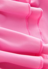 Heldere roze stof met een gladde textuur en golfachtige plooien. Bevat contrasterende stiksels langs de randen, wat een subtiel patroon creëert.