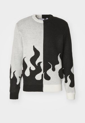 Sweter z dzianiny o podzielonym wzorze; jedna strona czarna, druga biała. Z wzorami płomieni w kolorze czarnym i białym wzdłuż dołu i rękawów.