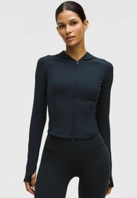 Tengerészeti sportkabát, testhez álló kialakítással, teljes hosszúságú cipzárral, kapucnival és hosszú ujjal, amelyen hüvelykujjnyílások találhatók. Az anyag sima és ruganyos.