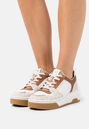 Baskets blanches et beige avec une tige texturée, comportant un design logo, un col rembourré et un système de laçage. Semelle en caoutchouc marron clair.