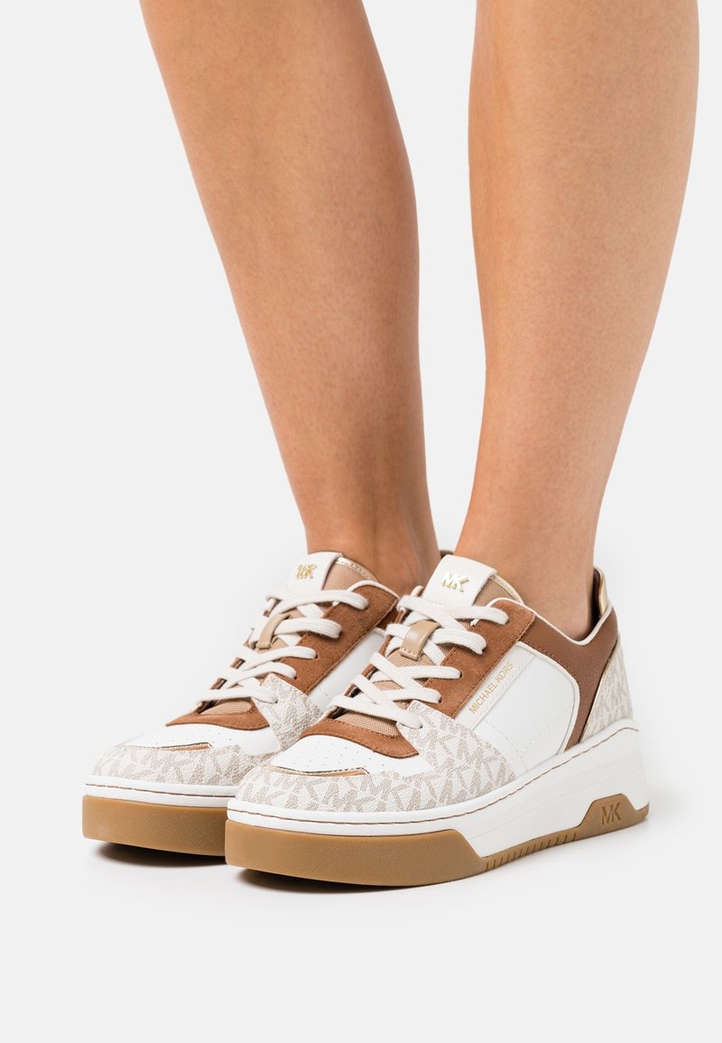 Sneaker bianchi e beige con parte superiore testurizzata, caratterizzate da un design con logo, collo imbottito e chiusura con lacci. Suola in gomma marrone chiaro.