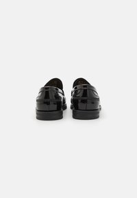 Loafers din piele lacuită neagră cu un finisaj elegant și lucios, având o cusătură decorativă și un spate moale, rotunjit. Talpă joasă din cauciuc texturat.
