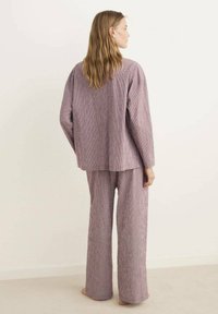 Tvådelad outfit i ett rosa och vitt rutmönster. Den löst sittande toppen har en rundad nederkant, och de vida byxorna når anklarna. Mjuk textur.