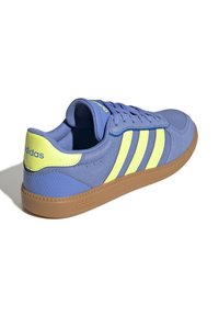 Zapatos deportivos de corte bajo con parte superior de textil azul, tres franjas amarillas llamativas y suela de goma con acentos texturizados.