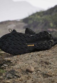 Zwarte wandelschoenen met robuuste Continental rubberzolen die rusten op rotsachtig buitenterrein met een vage natuurlijke achtergrond.