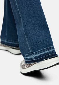 Wide-leg dark blue denim jeans with frayed hem, paired with patterned sneakers featuring a textured grey and white design.