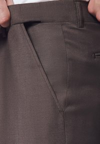 Brązowe spersonalizowane spodnie o strukturze w jodełkę, z boczną kieszenią i gładkim pasem, prezentujące czyste linie i dopasowany krój.