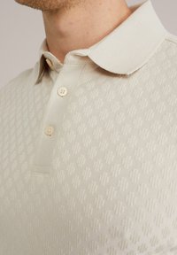 Beige polo shirt with a textured pattern, featuring a buttoned placket, soft collar, and fine ribbed accents.