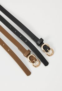 Due cinture in cuoio: una nera e una marrone. Entrambe hanno fibbie ovali in tonalità oro e fori distribuiti uniformemente per la regolazione. Texture piatta, design semplice.