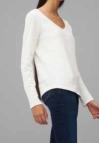 Vit långärmad skjorta med V-ringning, med en mjuk textur, rak passform och sidofickor, i kombination med mörkblå jeans.