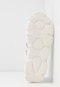 White sneaker sole featuring textured patterns with hexagonal shapes and herringbone grooves, designed for traction and durability.