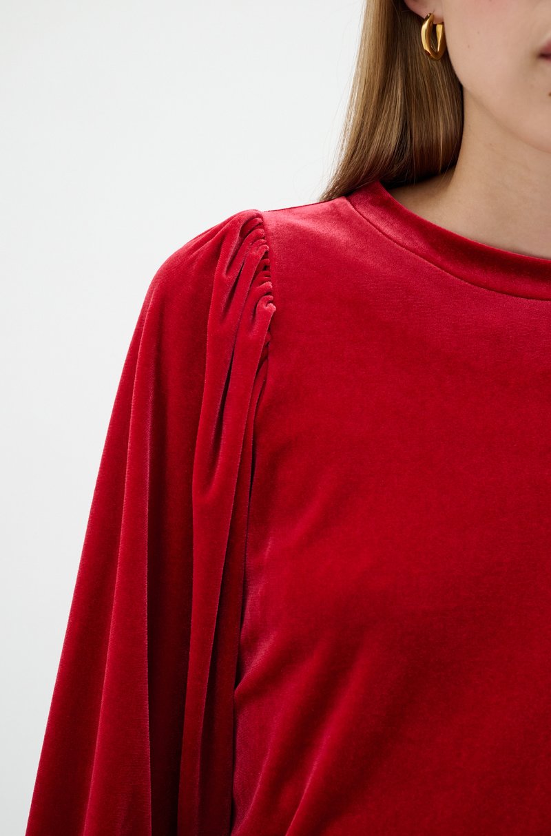 Rotes Samtoberteil mit plissierter Detailgestaltung an der Schulter und runder Ausschnitt. Glatte Textur mit einem weichen, luxuriösen Erscheinungsbild.