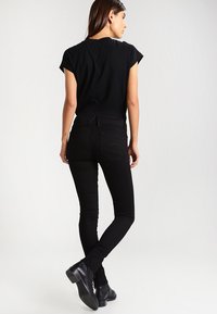Top negro de manga corta acompañado de jeans ajustados negros. El conjunto presenta una textura suave y un diseño entallado, complementado con botas de tobillo.