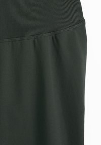 Tissu vert foncé avec une ceinture côtelée se transformant en une section inférieure à la texture lisse, soulignée par une couture horizontale.