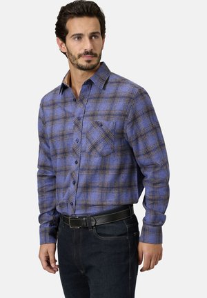 Karierte Flanellbluse in Blau und Braun mit einem Button-Down-Kragen, langen Ärmeln und einer Brusttasche, kombiniert mit dunklen Jeans und einem schwarzen Gürtel.