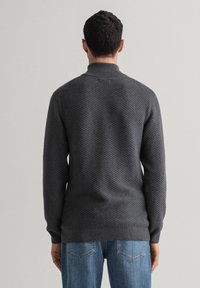 Pull en tricot gris foncé avec un motif texturé, col montant et poignets côtelés, associé à un jean bleu clair.