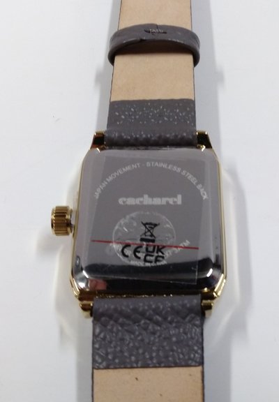 Vierkante horloge met gouden tint en een grijze leren band met structuur, met een roestvrijstalen achterkant gegraveerd met het merk "cacharel" en technische details.