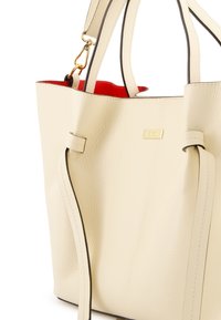Beige Leder-Tote mit schwarzem Besatz und goldenen Beschlägen. Verfügt über doppelte Griffe und ein lebhaft rotes Innenfutter. Texturierte Oberfläche mit minimaler Detailgestaltung.