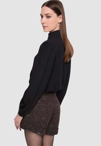 Blusa nera a collo alto abbinata a pantaloncini marroni scintillanti e texturizzati. Modella di profilo, capelli lisci, sfondo chiaro.