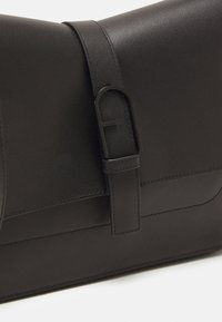Borsa a mano in pelle nera con forma rettangolare, texture liscia e un evidente fermaglio in metallo nero con dettaglio del logo.
