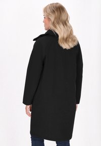 Ilgas juodas paltas su lygiu paviršiumi, smailiu apykakle ir šoniniais kišeniais. Turi tiesias rankoves ir yra vidutinio ilgio, siekiantis iki šlaunies.