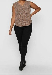 Kwiatowa bluzka z dekoltem w serek i krótkimi rękawami w ziemistych odcieniach, zestawiona z czarnymi obcisłymi dżinsami i czarnymi botkami na obcasie. Gładka faktura materiału.