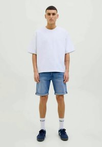 Witte oversized T-shirt, lichtblauwe denim shorts, marineblauwe sneakers en witte crew sokken. Eenvoudig ontwerp, ontspannen pasvorm. Soepele stoftexturen.