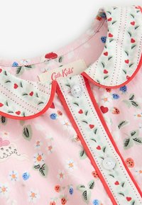 Roze kinderblouse met een witte gegolfde kraag, rode hart- en bladmotieven, bloemen- en lieveheersbeestjesprints, en witte knopen aan de voorkant.