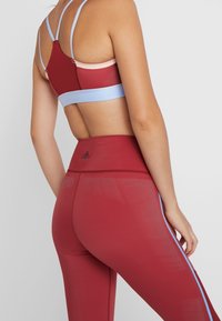 Sport bh med smalle stropper i rød, pink og blå; matchende højtaljede leggings i rød med blå sidelister og teksturerede detaljer.