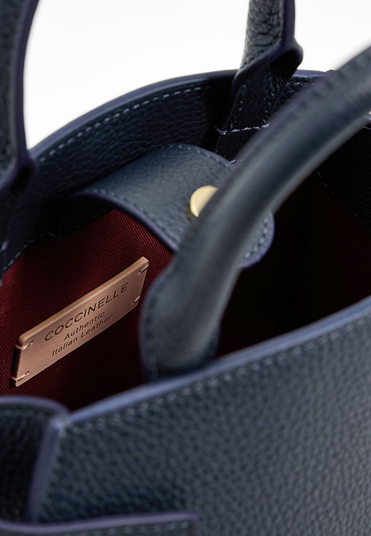 Borsa in pelle blu navy con esterno texturizzato. L'interno presenta una fodera rossa e un'etichetta con la scritta "Coccinelle Authentic Italian Leather."