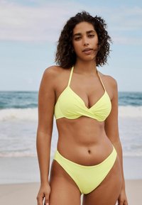 Žuti bikini set koji se sastoji od halter topa s uvijenim prednjim dijelom i odgovarajućim visokim gaćicama, izrađen od glatkog materijala, dizajniran za udoban fit.