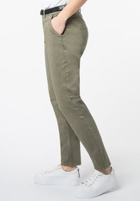 Olijfgroene broek met een slim fit, voorzakken en subtiele stikseldetails, gecombineerd met witte platform sneakers.