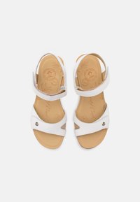 Sandalias blancas con correas ajustables, hechas de un material similar al cuero suave, diseño de punta abierta y una plantilla acolchada de color marrón claro.