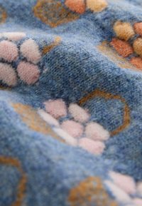 Tissu tricoté doux avec un fond bleu présentant des motifs floraux géométriques roses et oranges dans une texture duveteuse.