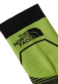 Calcetín verde con detalles en negro, que presenta una tela texturizada, el logo de The North Face y un diseño a rayas en el puño.